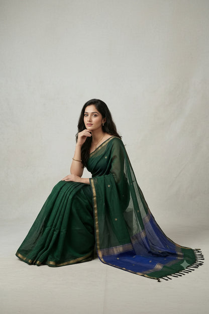 Woman wearing a green saree with a blue border on a light gray background