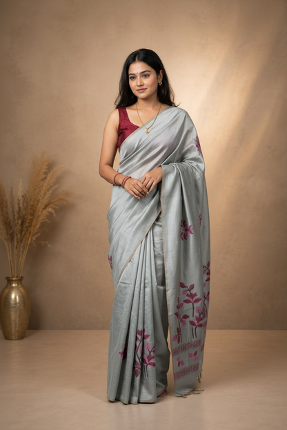Woman wearing a light grey saree with floral patterns against a beige background
