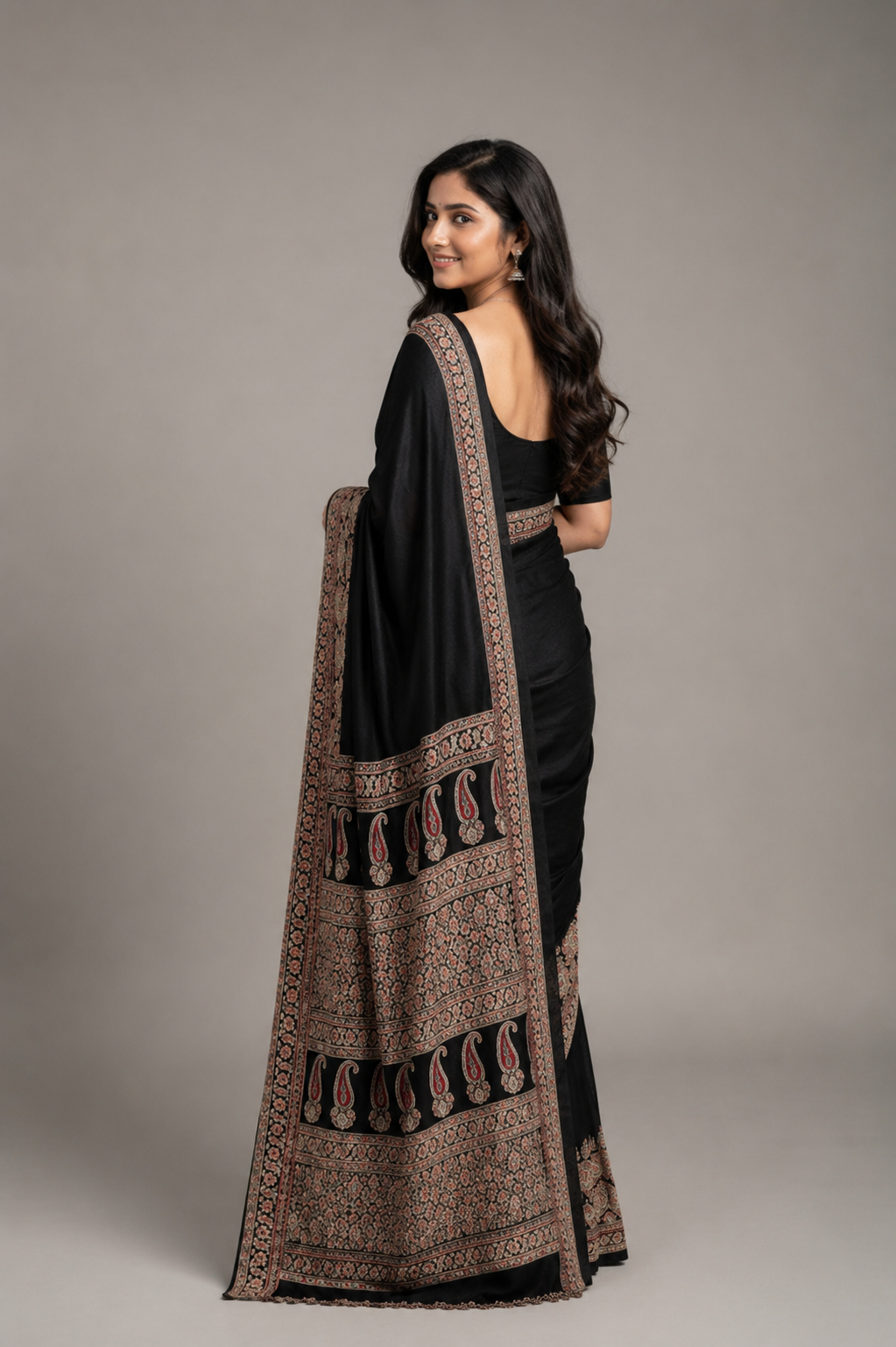 Woman wearing a black saree with a patterned border against a plain background