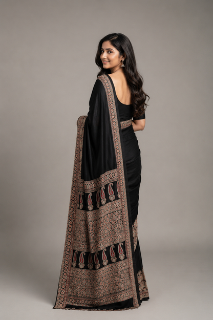 Woman wearing a black saree with a patterned border against a plain background