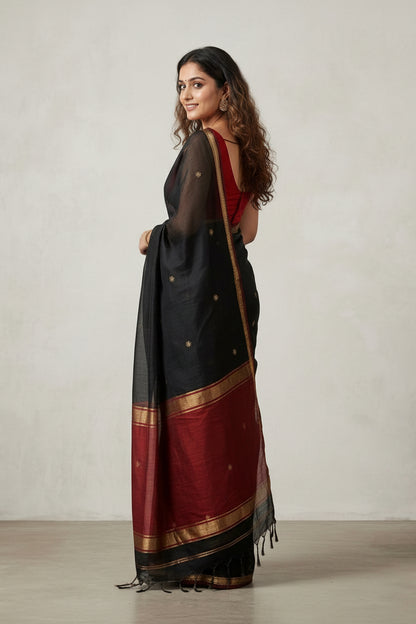 Woman wearing a black saree with gold and red accents on a plain background