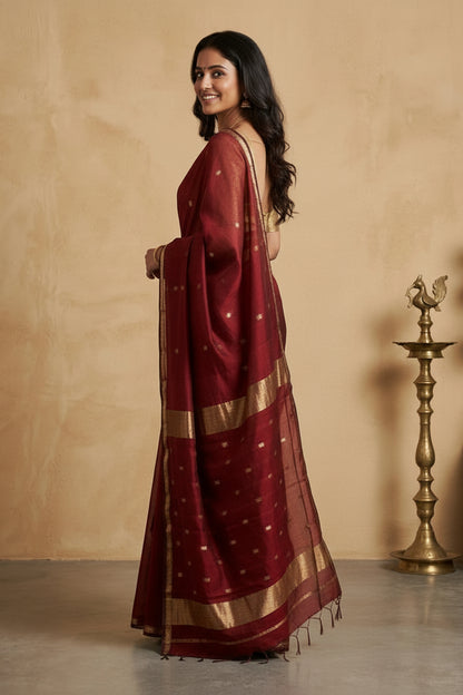 Woman wearing a maroon saree with gold border against a beige background